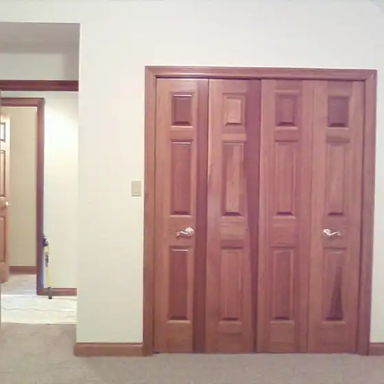 A pair of paneled wood bifold closet doors with lever handles in a finished stained wood frame