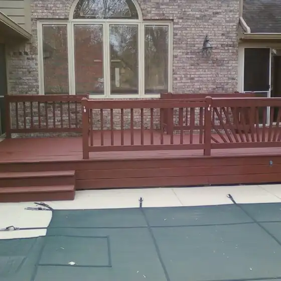 Red-brown stained deck with a matching railing and two steps, set beside a pool cover
