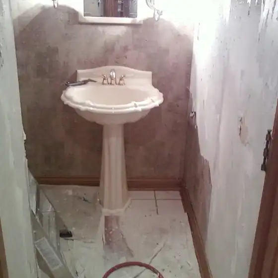 Half bath stripped back with a pedestal sink and bare patched walls