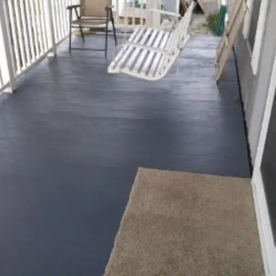 Porch floor coated in dark blue-grey paint with a white porch swing, a folding chair and a tan mat