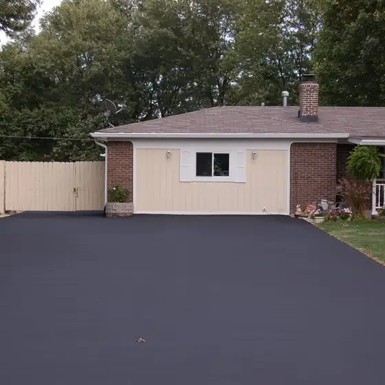 Freshly sealcoated black asphalt driveway leading to a cream detached garage