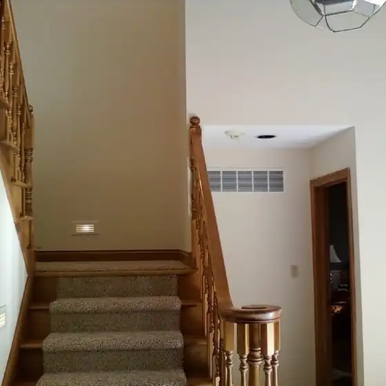 Finished carpeted staircase with a stained wood handrail and painted walls